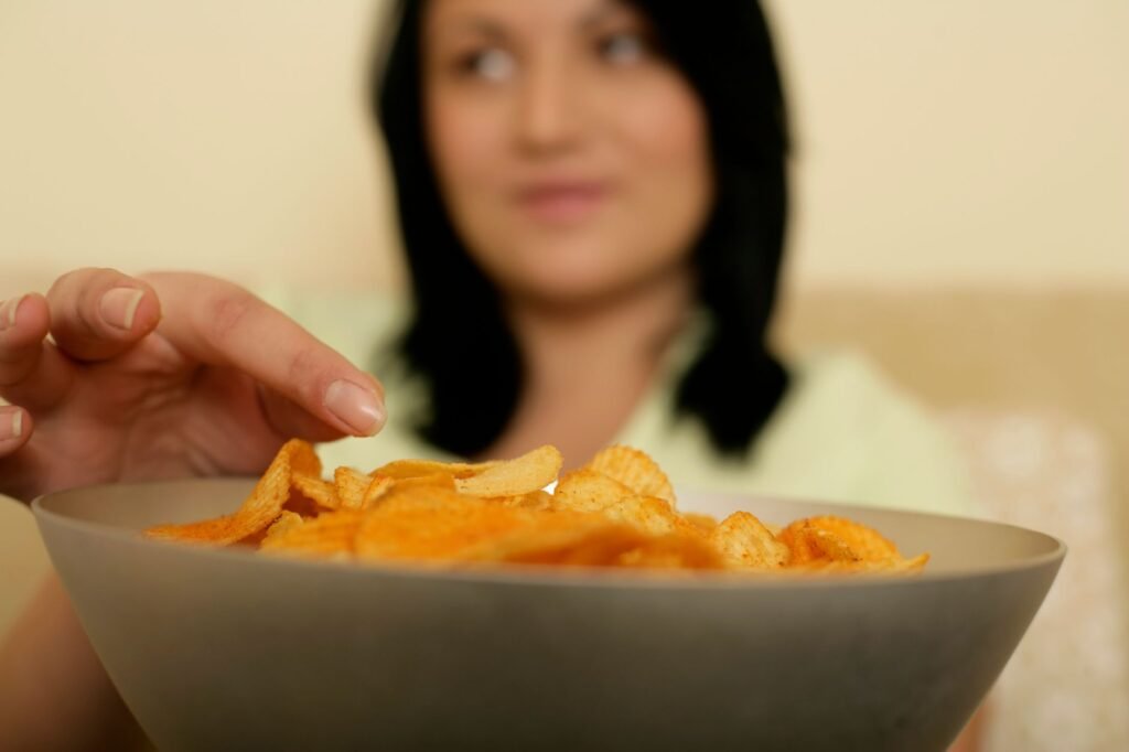 A woman reaching for a bowl full of crispy potato chips, capturing a moment of indulgence.