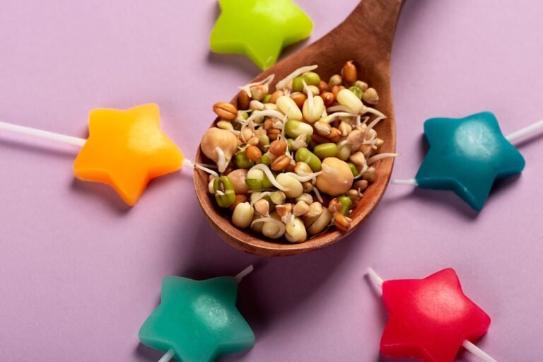 Close-up of healthy sprouts in a wooden spoon surrounded by colorful star-shaped candies on a purple surface.