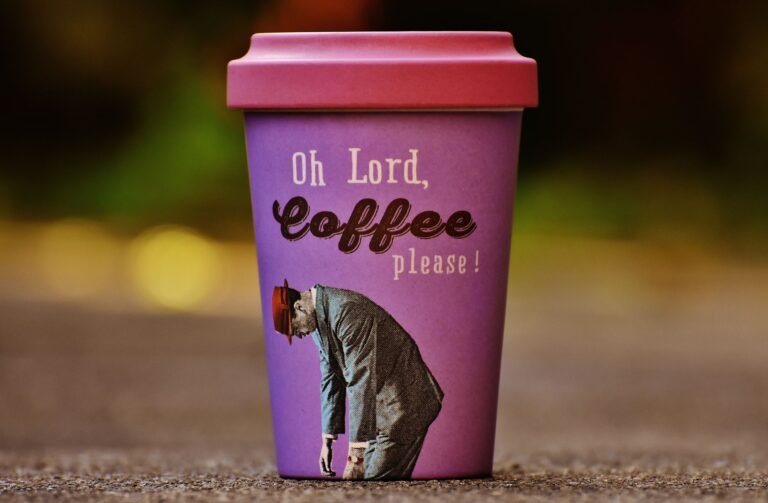 Purple coffee cup with humorous text 'Oh Lord, Coffee please!' placed outdoors on a blurred background.