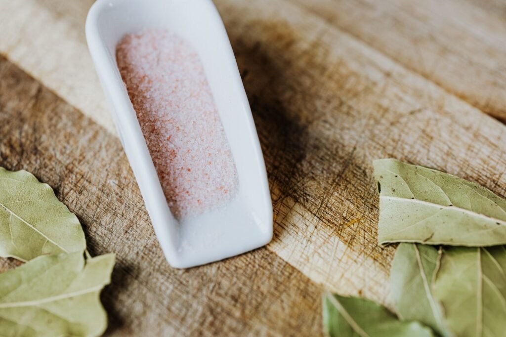 Close-up of pink Himalayan salt and bay leaves on a rustic wooden surface, highlighting natural ingredients.