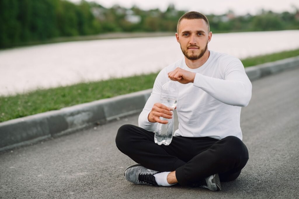 Man sitting on a road side, taking a break with a water bottle during an outdoor workout.