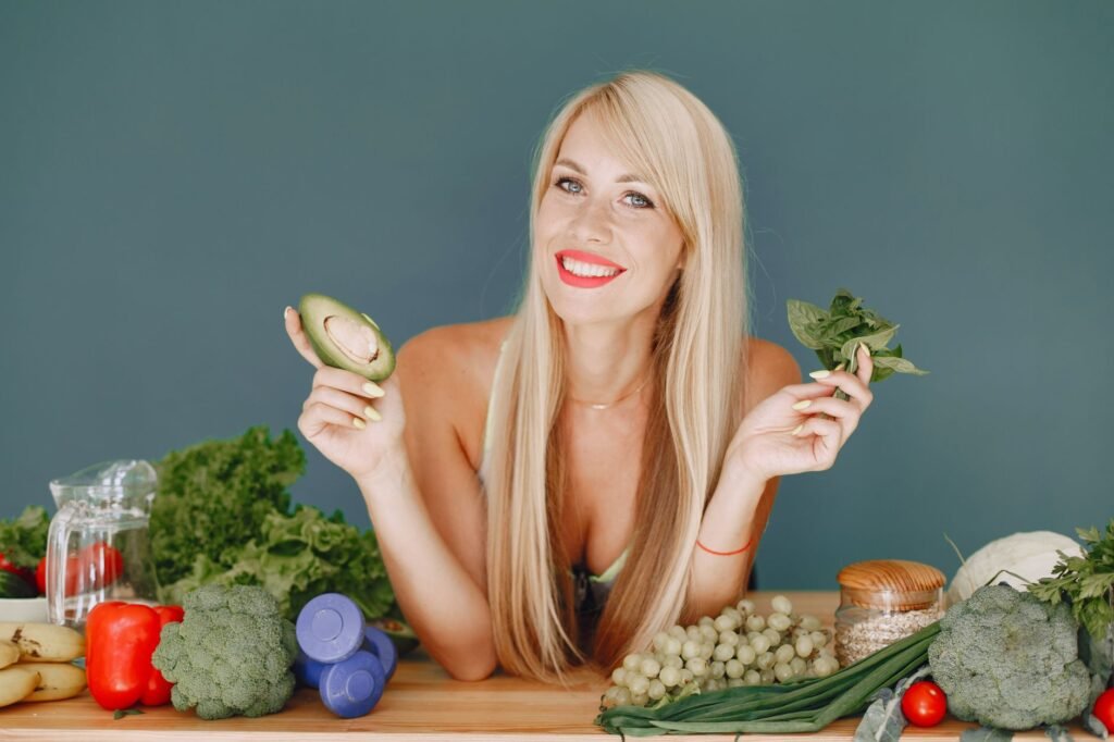 Blonde woman promotes healthy eating with fresh vegetables and fruits on display.