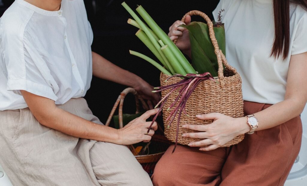 Crop unrecognizable female partners with fresh vegetables and herbs in wicker basket resting near car