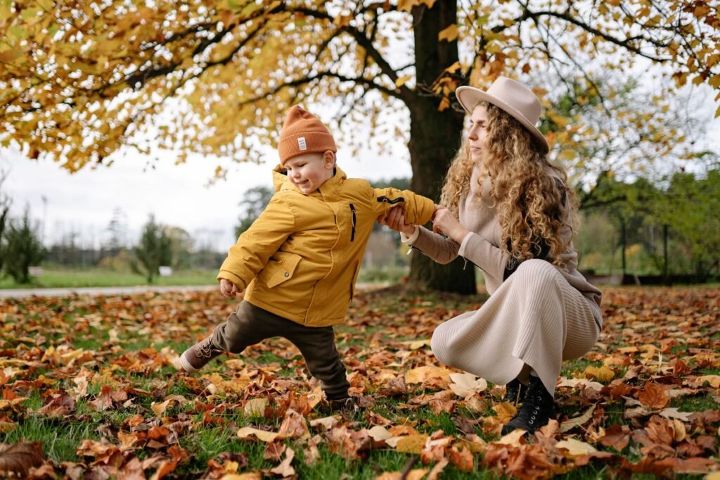 Joyful mother and child play in a park filled with colorful autumn leaves.