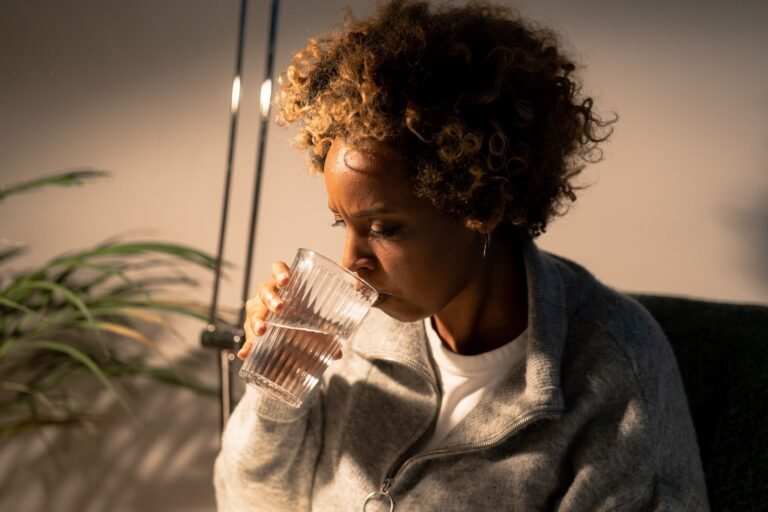 Portrait of an African American woman savoring a refreshing glass of water indoors.
