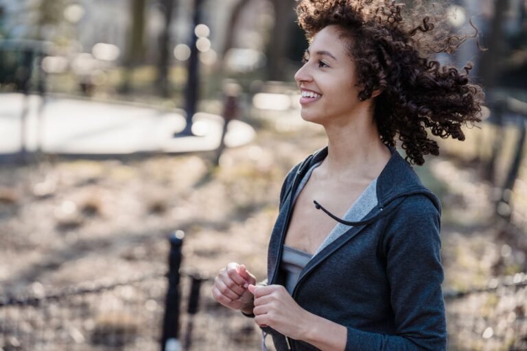 Side view of young African American female smiling while running in park against blurred background