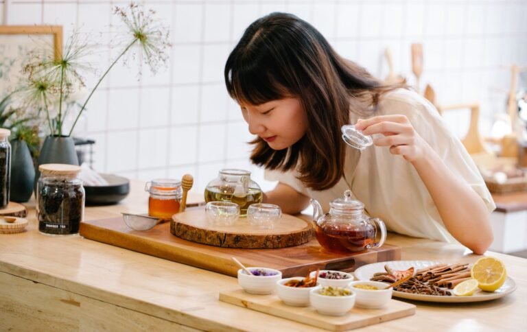 Woman preparing herbal tea with natural ingredients in a kitchen setting, focusing on aroma and presentation.