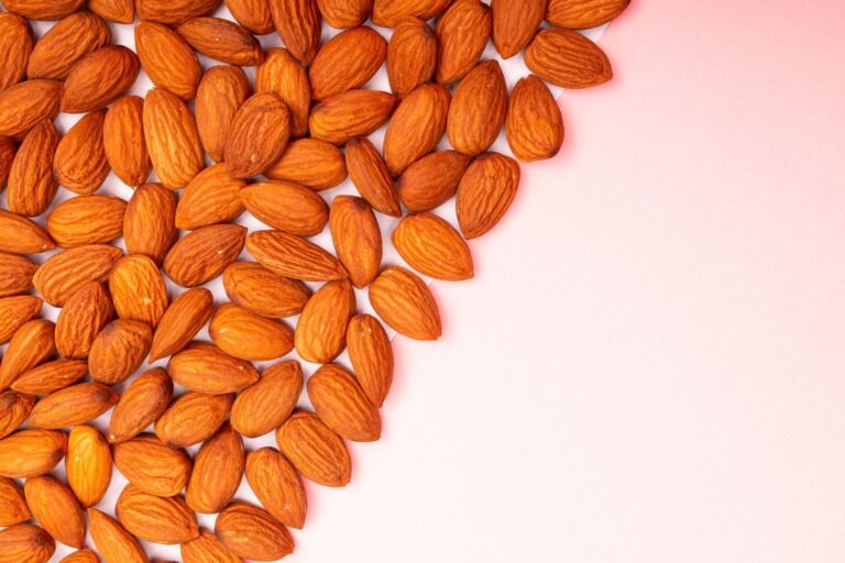 Organic almonds arranged on a pastel pink surface, perfect for health and nutrition themes.
