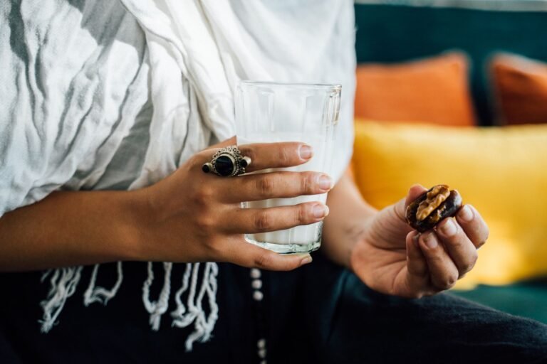 A close-up image showing hands holding a glass of milk and a date, symbolizing Iftar.