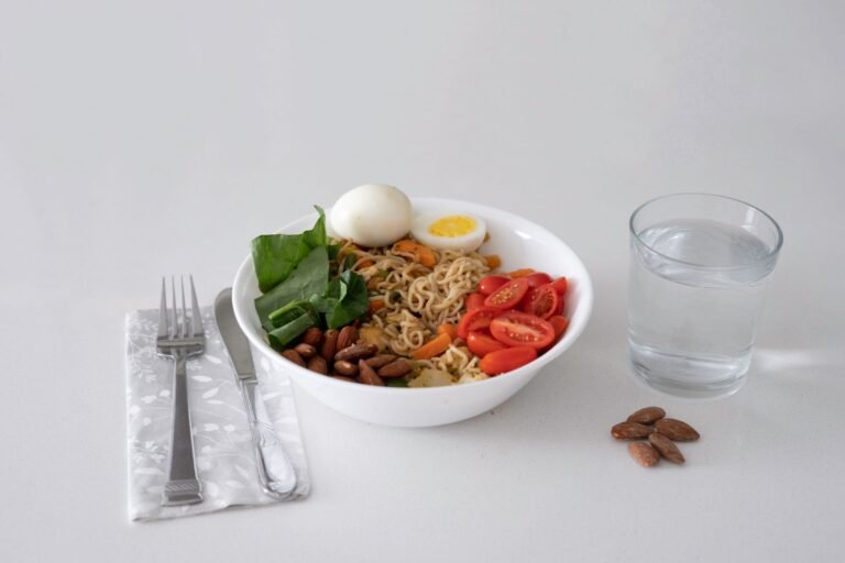A nutritious bowl of noodles with eggs, vegetables, almonds, and a glass of water.