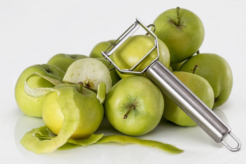 A group of fresh green apples with a stainless steel peeler on a white background.