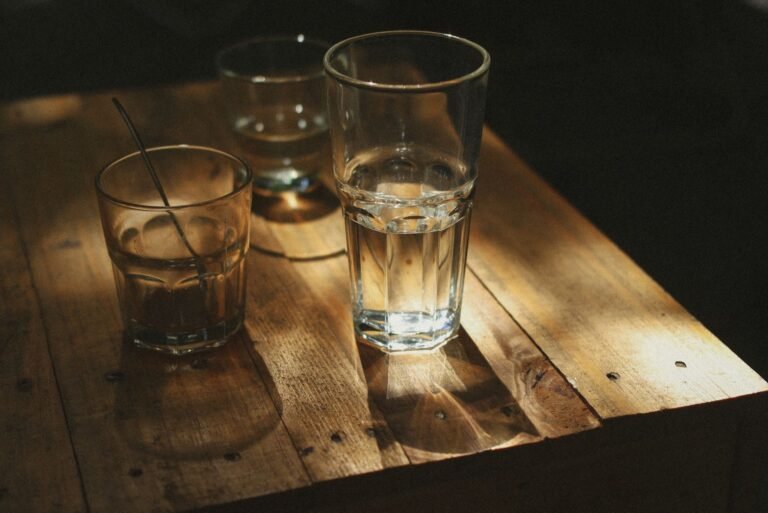 A warm, dramatic still life of drinking glasses casting shadows on a wooden table.
