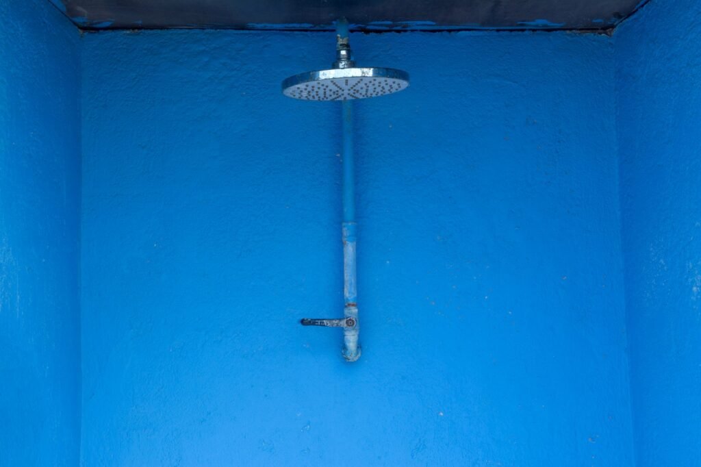 Blue textured shower area with single metal rain shower head against a vibrant wall.