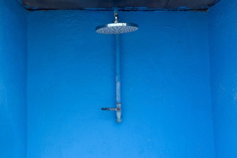 Blue textured shower area with single metal rain shower head against a vibrant wall.