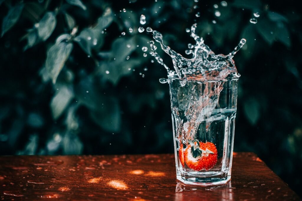 A vibrant strawberry splashes into a glass of water, captured mid-motion.