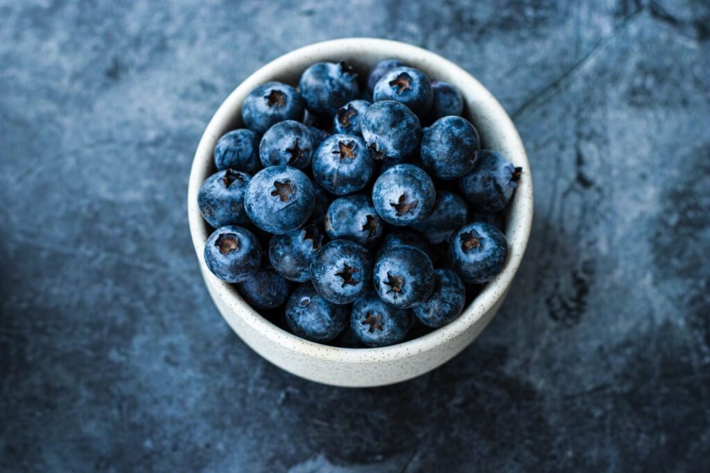 A close-up shot of blueberries in a white bowl on a dark textured background, emphasizing fresh, healthy eating.