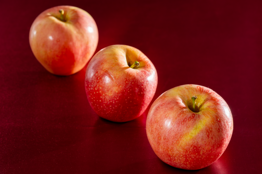 Three fresh red apples on a deep red background emphasizing health and vitality.