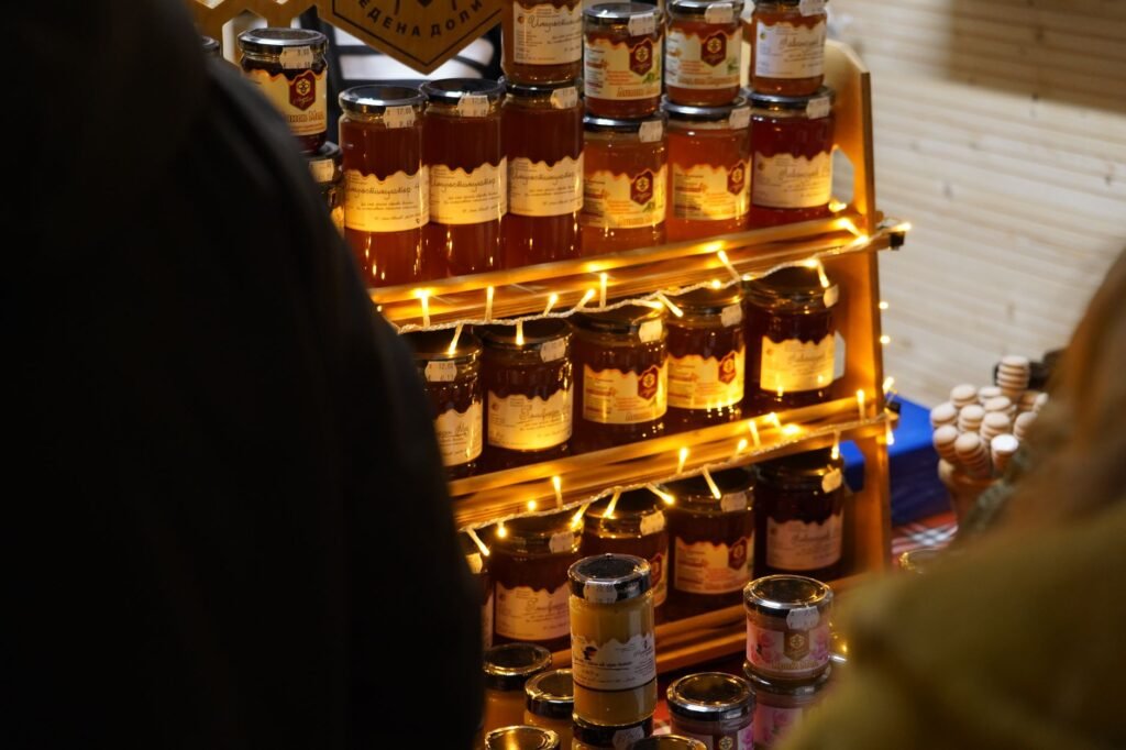 A cozy display of various honey jars lit with warm fairy lights at a market.