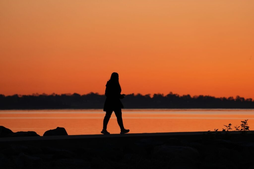 A serene silhouette of a woman strolling by a lake during a vibrant sunset.