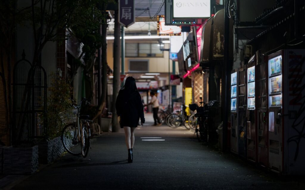 A woman walks down a dimly lit street in Osaka, Japan, lined with vending machines.