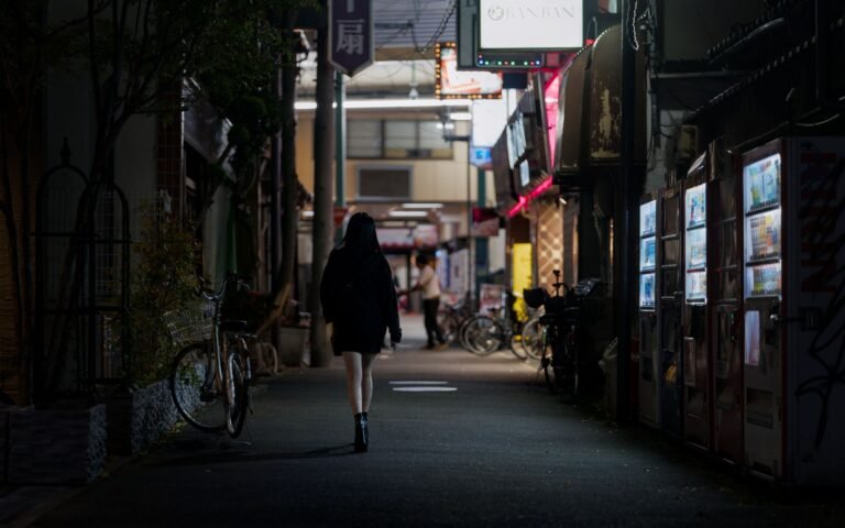 A woman walks down a dimly lit street in Osaka, Japan, lined with vending machines.