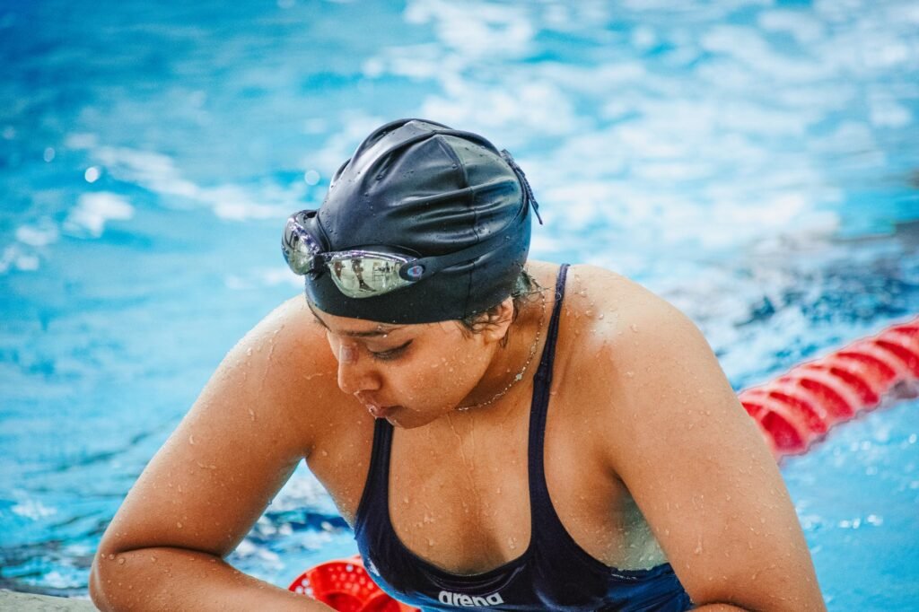 Female swimmer in swim cap and goggles resting poolside, focused and determined.