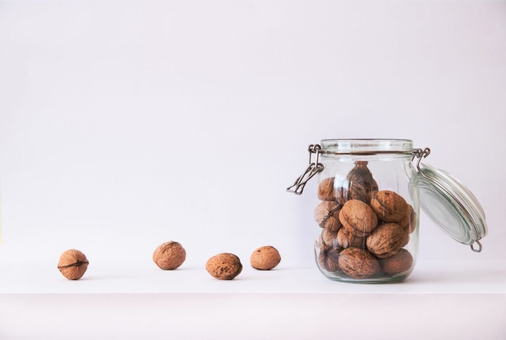 A collection of walnuts in a glass jar with scattered nuts on a white background, showcasing simplicity and nutrition.