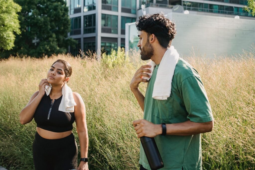 Two adults cooling down after exercise in an urban park setting, enjoying a summer day.