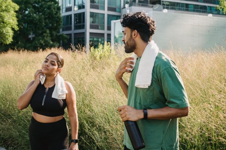 Two adults cooling down after exercise in an urban park setting, enjoying a summer day.