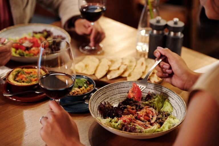 A group enjoying gourmet salads and red wine in an elegant restaurant setting.
