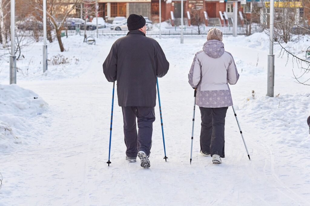 Elderly couple enjoying a winter walk with ski poles in a snowy park setting.