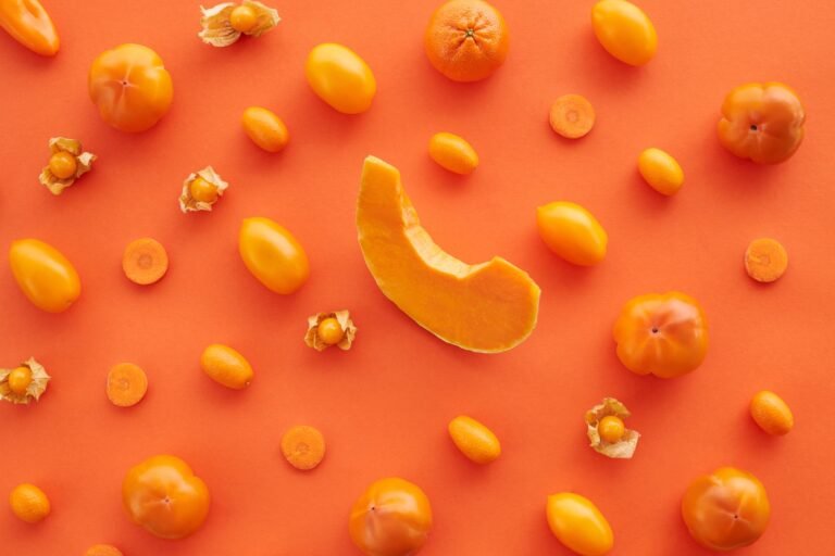 Top view of assorted orange fruits and vegetables on orange surface, offering organic health benefits.