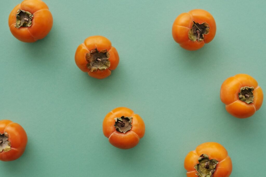 Flat lay of fresh persimmons on a green background, highlighting their natural vibrancy.