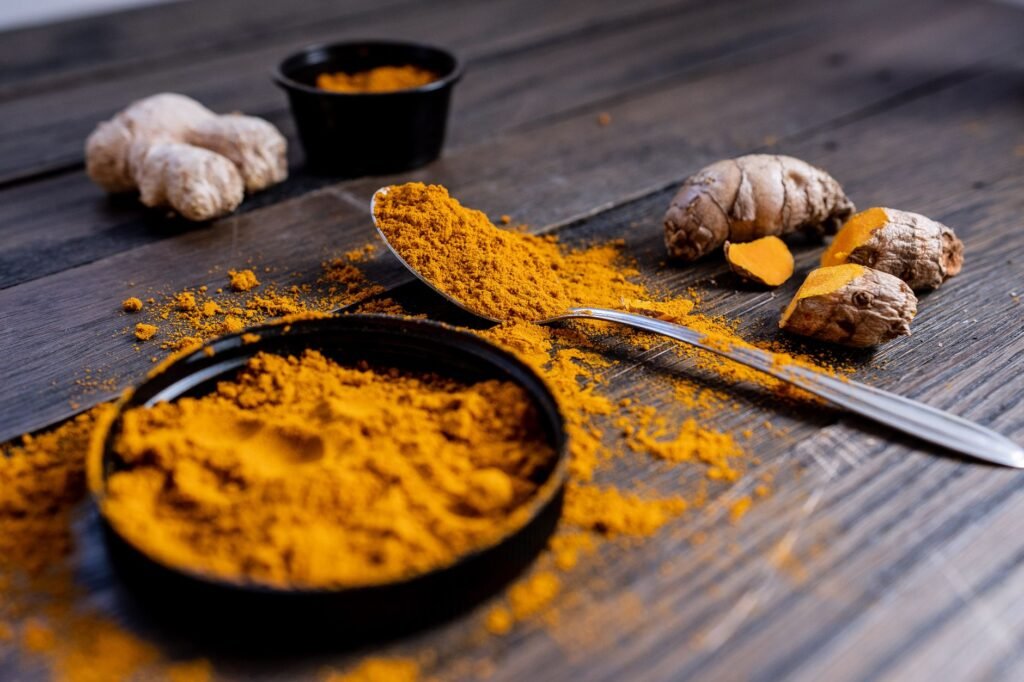 Vibrant turmeric powder and root arranged on a rustic wooden surface, showcasing culinary spice ingredients.