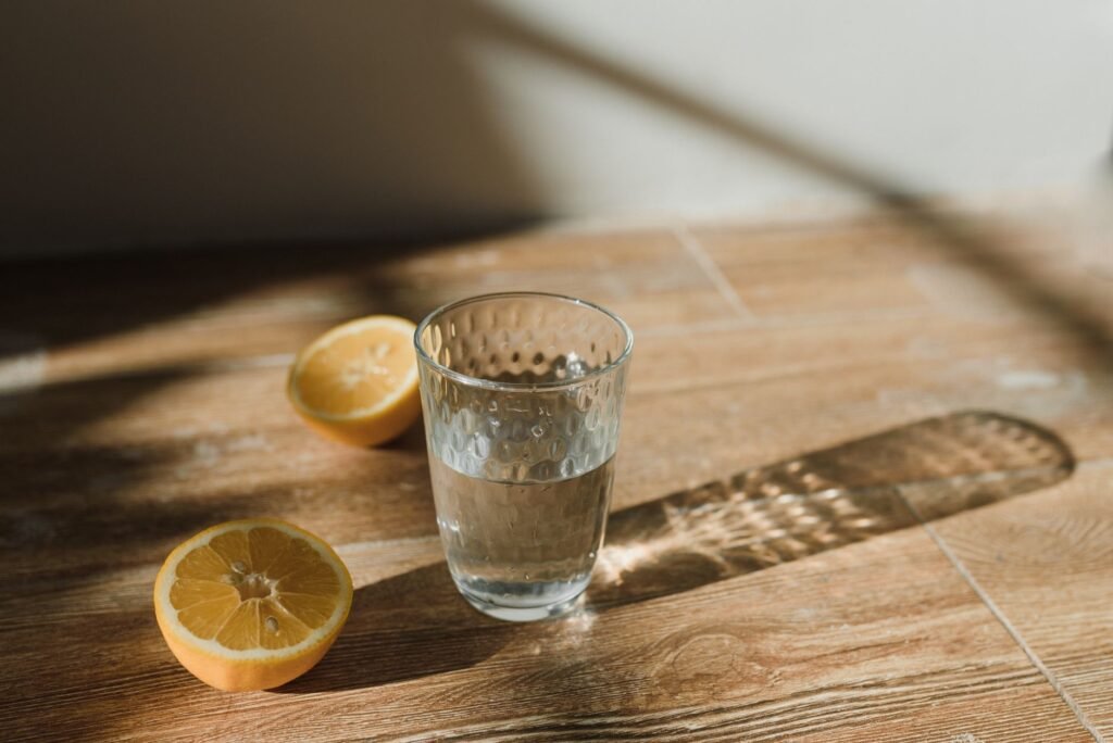 Clear glass of water with sliced lemons on a wooden surface in natural sunlight.
