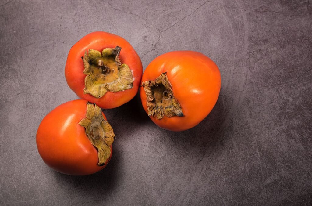 Top view of three fresh ripe persimmons on a gray textured surface, perfect for autumn harvest themes.