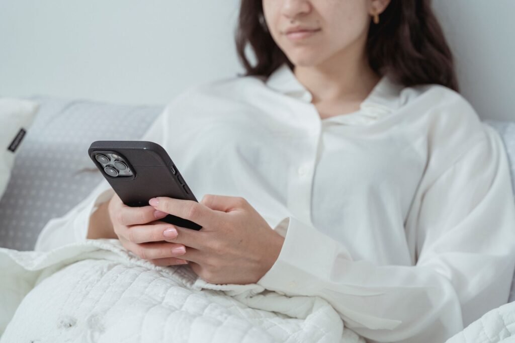 Young woman relaxing in bed while using a smartphone, enjoying leisure time indoors.