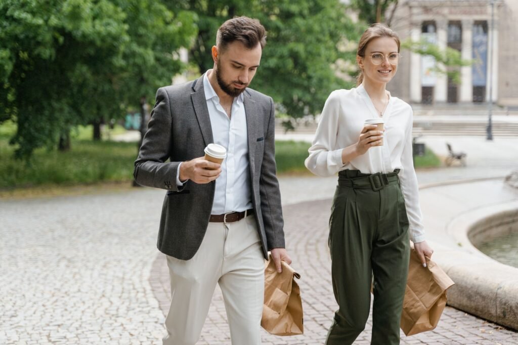 Professional colleagues walking with coffee and bags in a park setting.