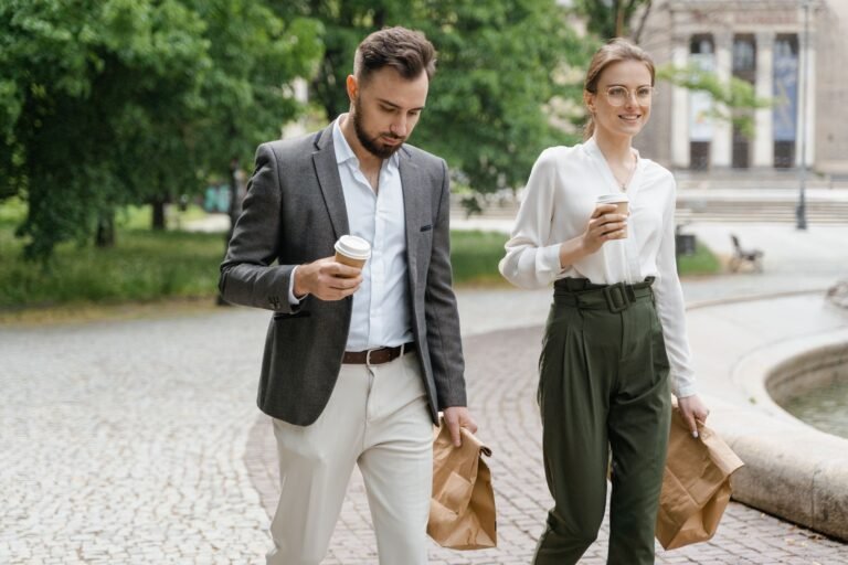 Professional colleagues walking with coffee and bags in a park setting.