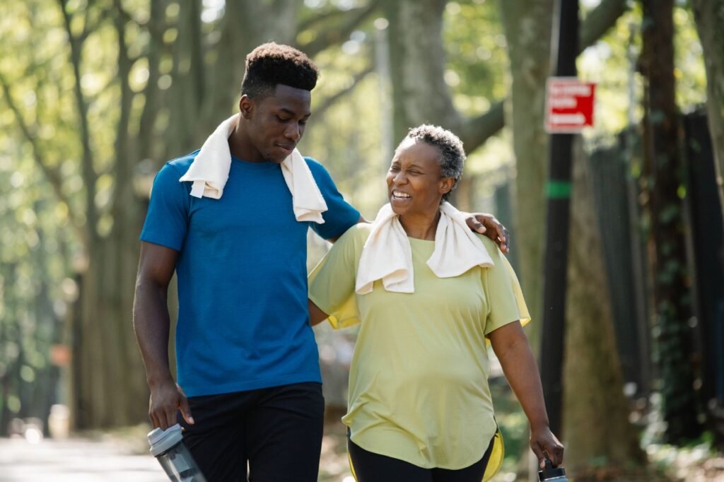 An elderly woman and young man walk arm in arm, smiling in a park. Active lifestyle.
