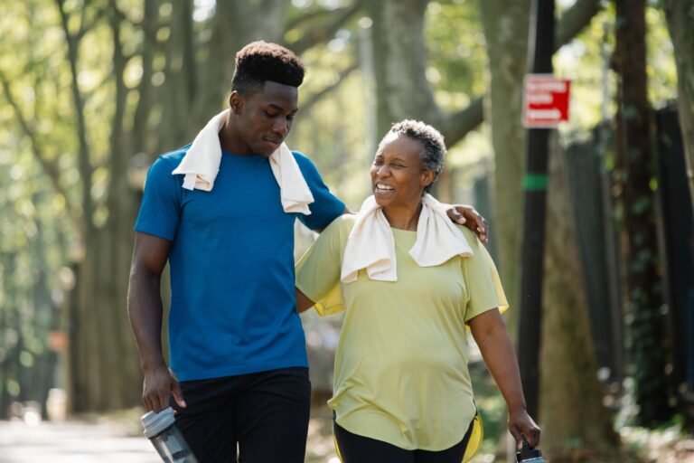 An elderly woman and young man walk arm in arm, smiling in a park. Active lifestyle.