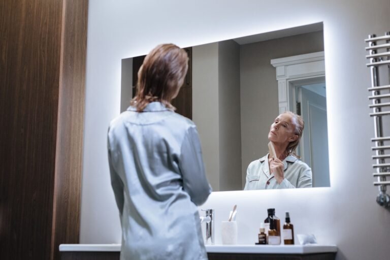 Elderly woman in pajamas begins her day with self-care in a modern bathroom mirror.