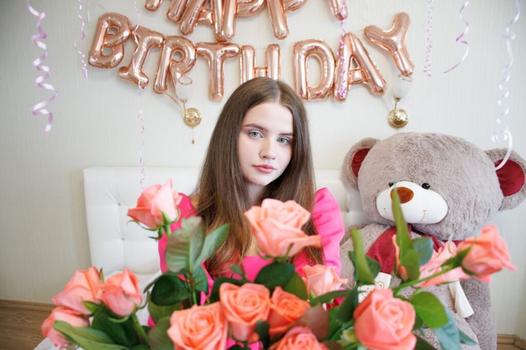 Young woman celebrating birthday with roses and a giant teddy bear, indoors.