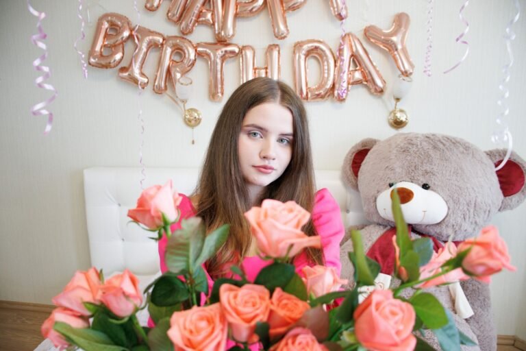Young woman celebrating birthday with roses and a giant teddy bear, indoors.