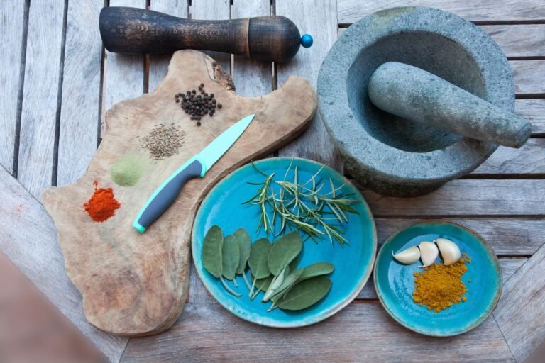 A rustic setup for spice preparation with herbs, spices, garlic, and kitchen tools on wooden table.