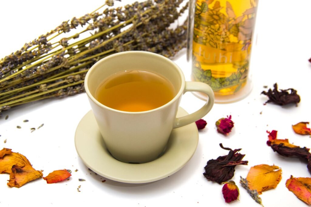 A soothing herbal tea in a cup surrounded by colorful dried flowers and a lavender bouquet on a white backdrop.