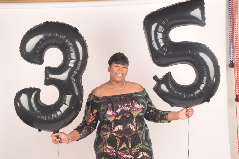 A joyful woman holding giant 35 balloons, celebrating a milestone birthday indoors.