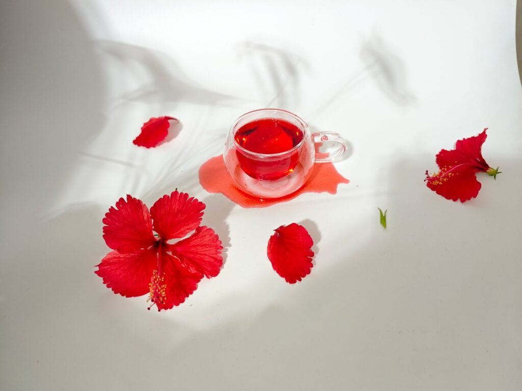 Glass of hibiscus tea with vibrant red petals on a white background, inviting refreshment and beauty.