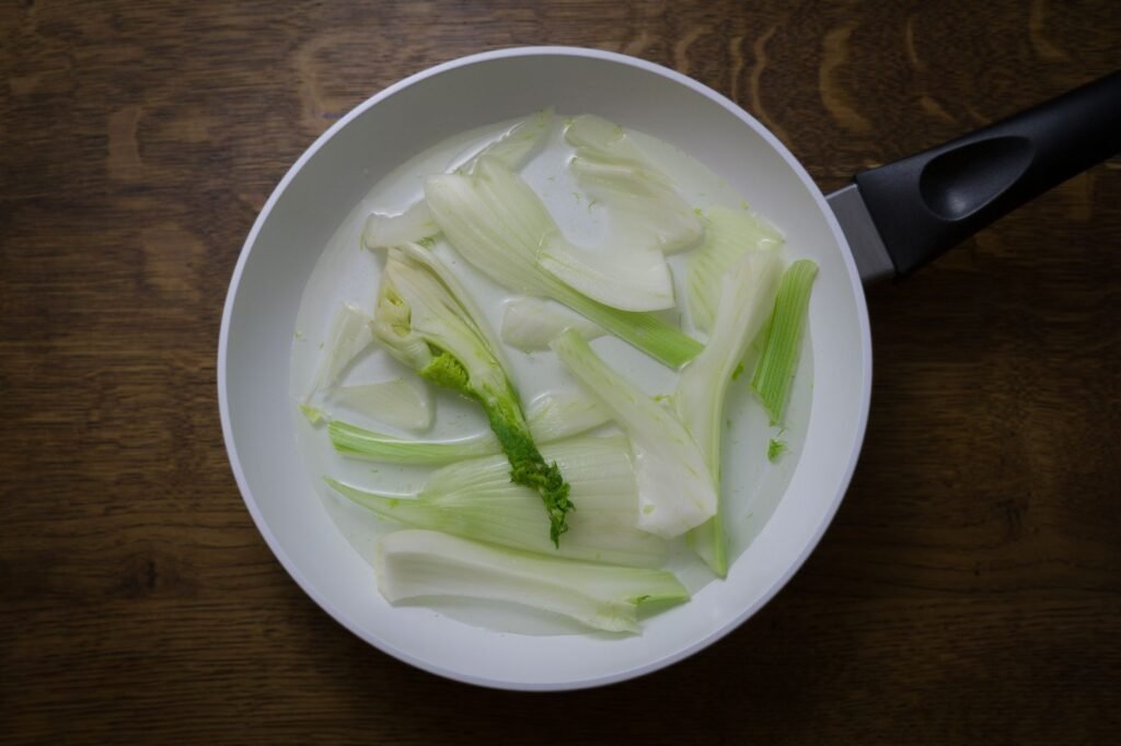 Overhead view of fresh fennel slices in a white frying pan. Perfect for healthy cooking concepts.