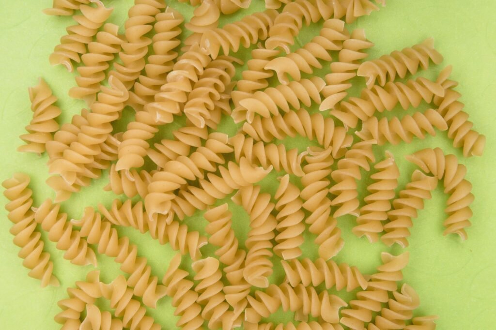 Uncooked rotini pasta spirals scattered on a bright green surface, ideal for culinary themes.